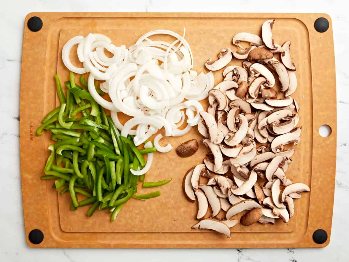 Peppers, onion and sliced mushrooms on a cutting board.