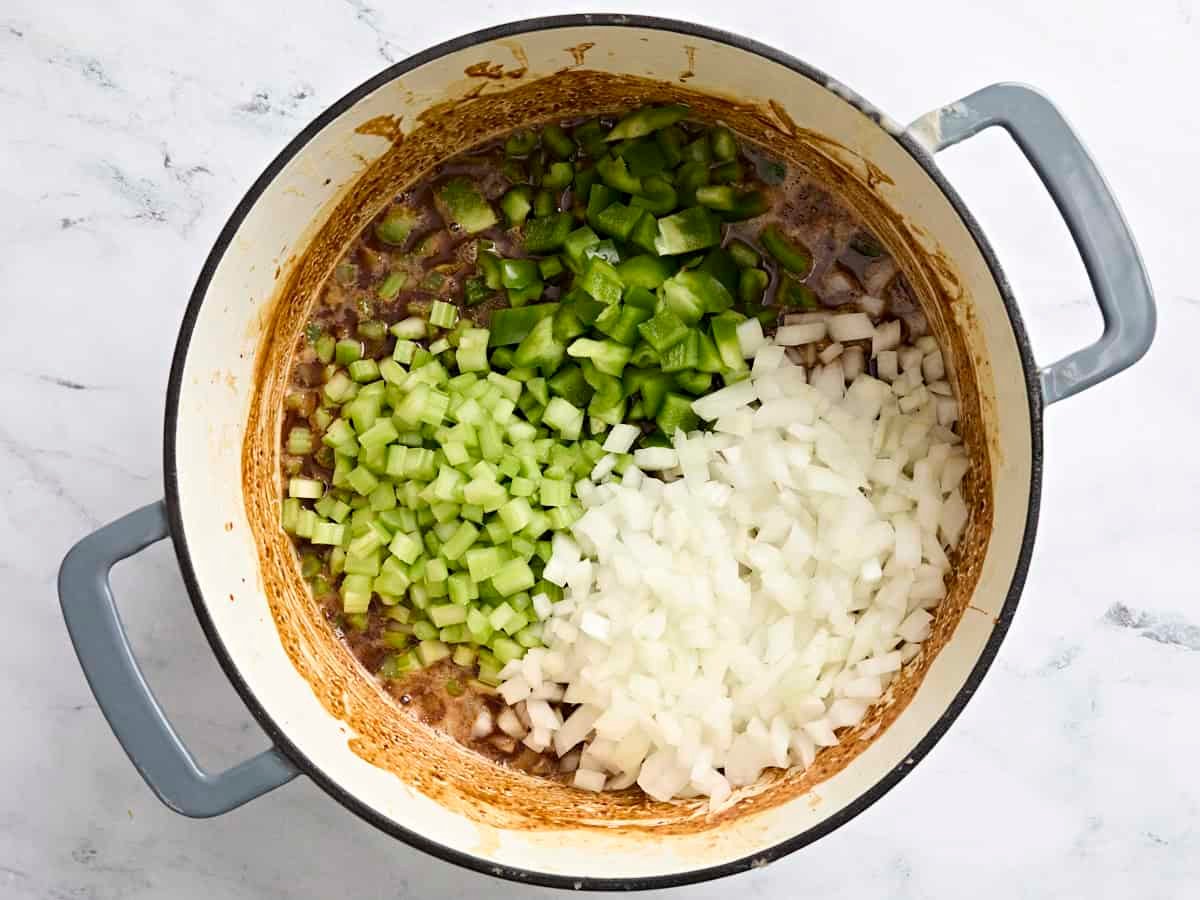 Diced bell pepper, onion, and celery in a dark brown roux in a pot.