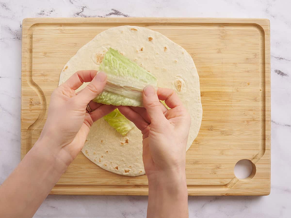 A hand straightening a piece of lettuce before putting it on a wrap.
