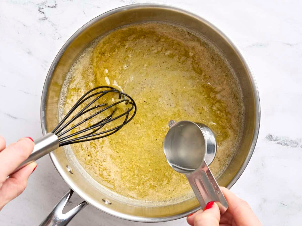 Reserved pasta water being whisked into melted butter in a skillet.