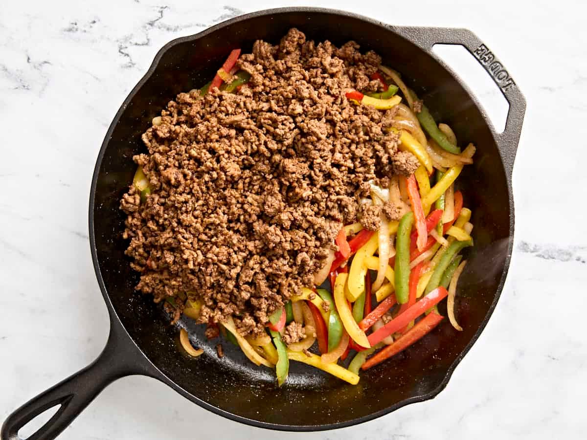 Sliced peppers added to browned ground beef in a skillet.