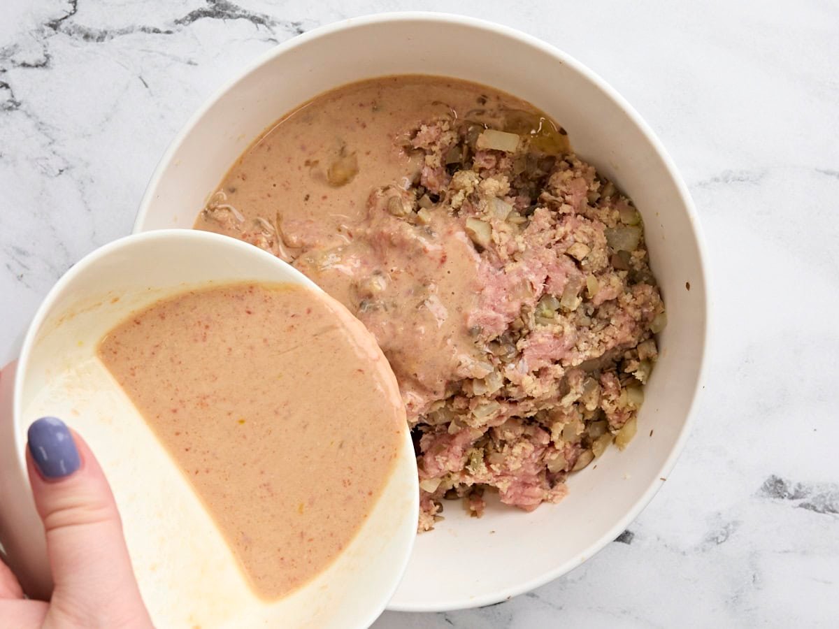 The wet egg and milk mix being poured into a bowl of ground turkey, veggies, and breadcrumbs.