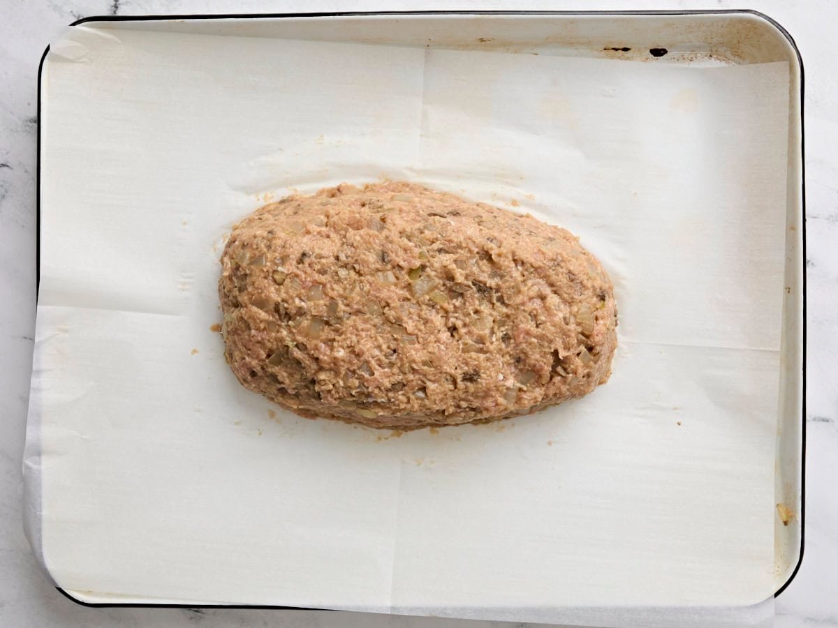 The meat mix for turkey mushroom meatloaf formed into a loaf on a parchment lined baking sheet.