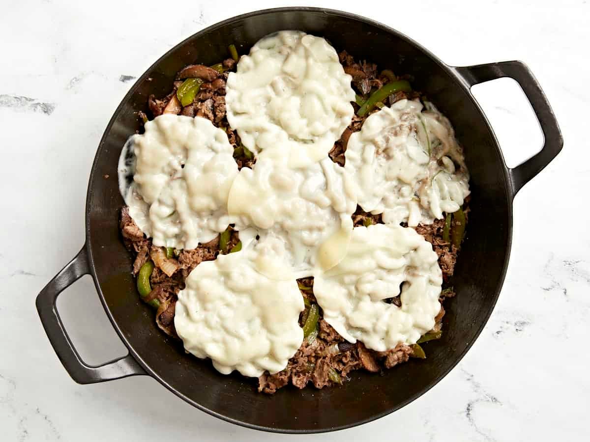 Provolone cheese added on top of cooked cheesesteak in skillet.