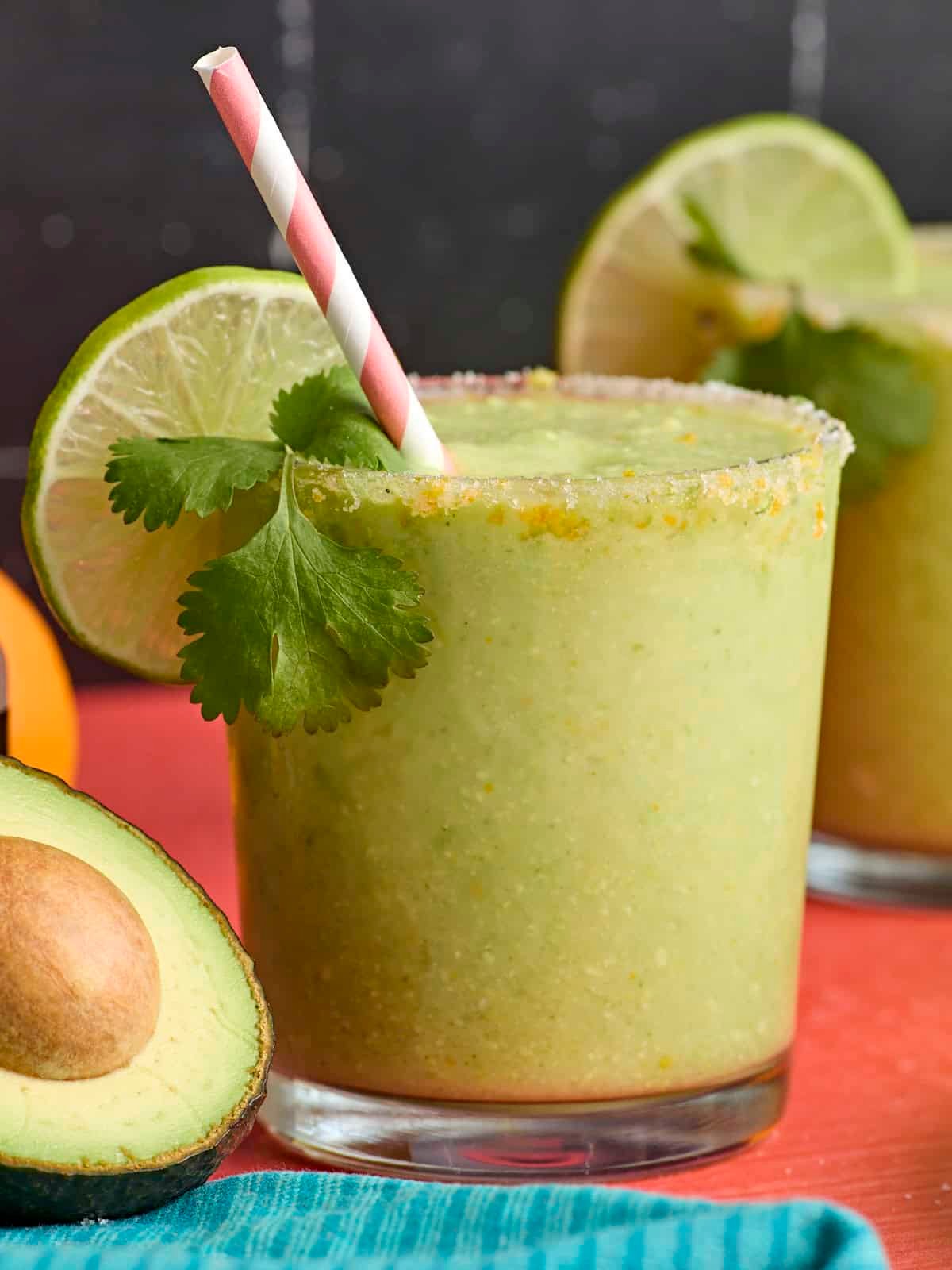 Side view of a glass of avocado margarita, garnished with lime slices and fresh cilantro.