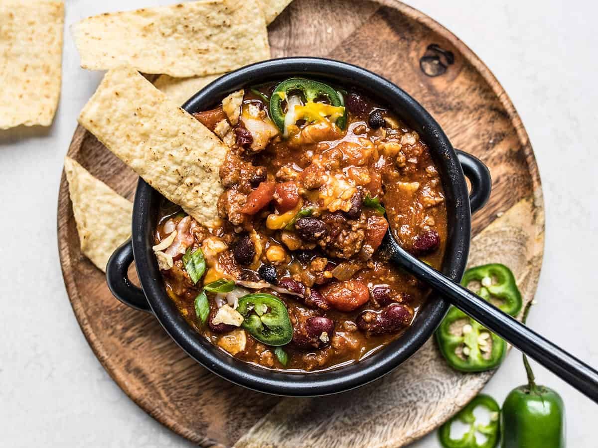 Overhead view of a bowl full of chili with toppings and a spoon in the center.