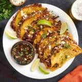 Overhead view of a plate of beef birria tacos with a bowl of consome.