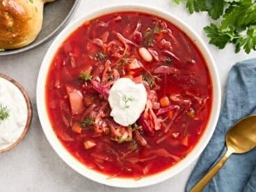 Overhead view of a bowl of borscht topped with sour cream and fresh herbs.