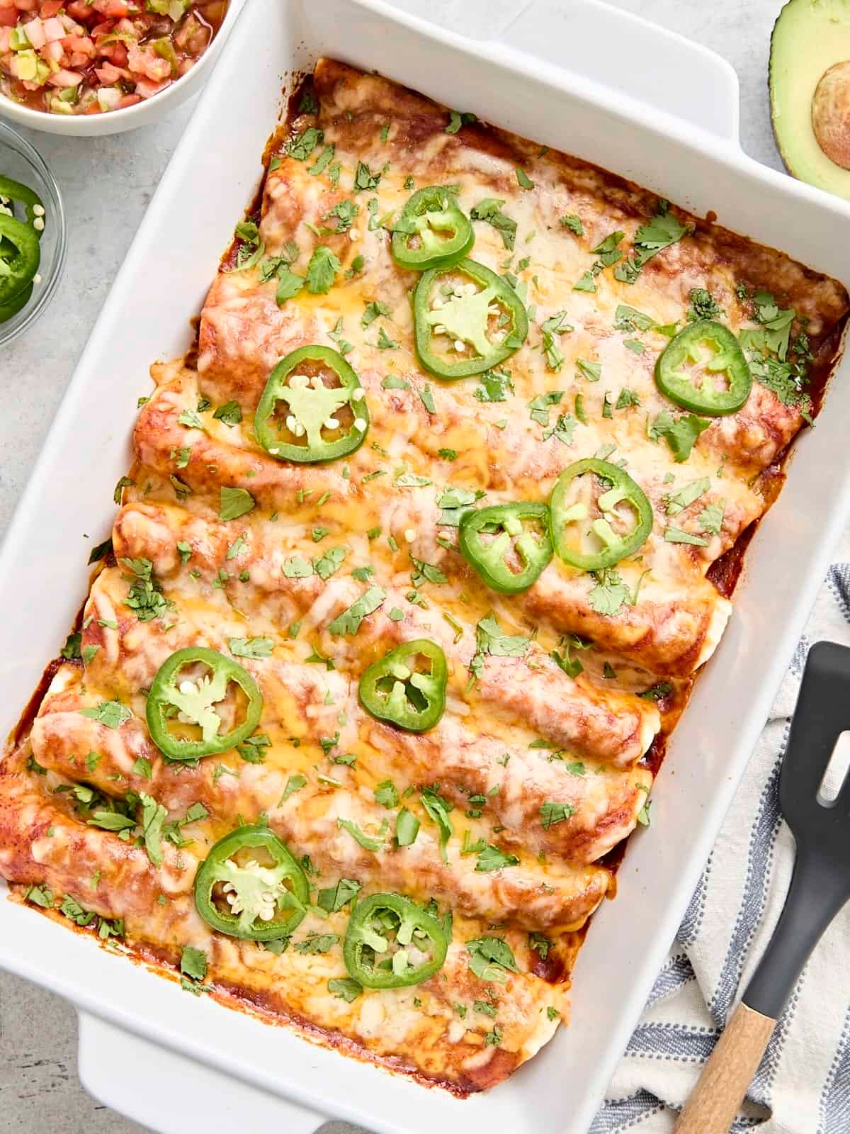 Overhead view of chicken enchiladas in a baking dish topped with fresh cilantro and sliced jalapenos.