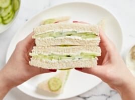 Side view of hands holding a stacked cucumber sandwich.