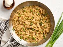 Overhead view of garlic noodles in a skillet, topped with sliced green onions.