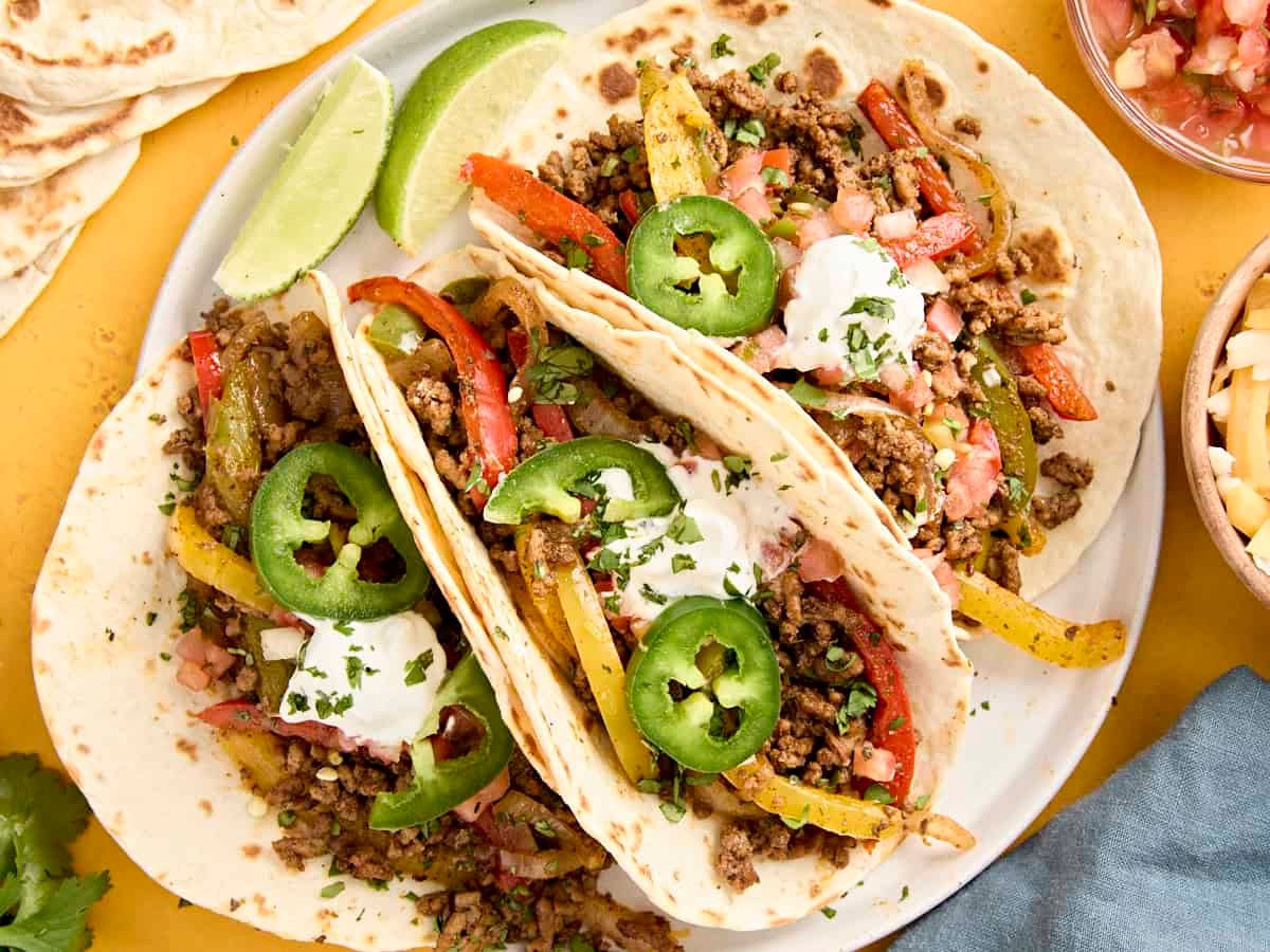 Overhead view of ground beef fajitas on a plate, topped with sour cream and jalapeno slices.