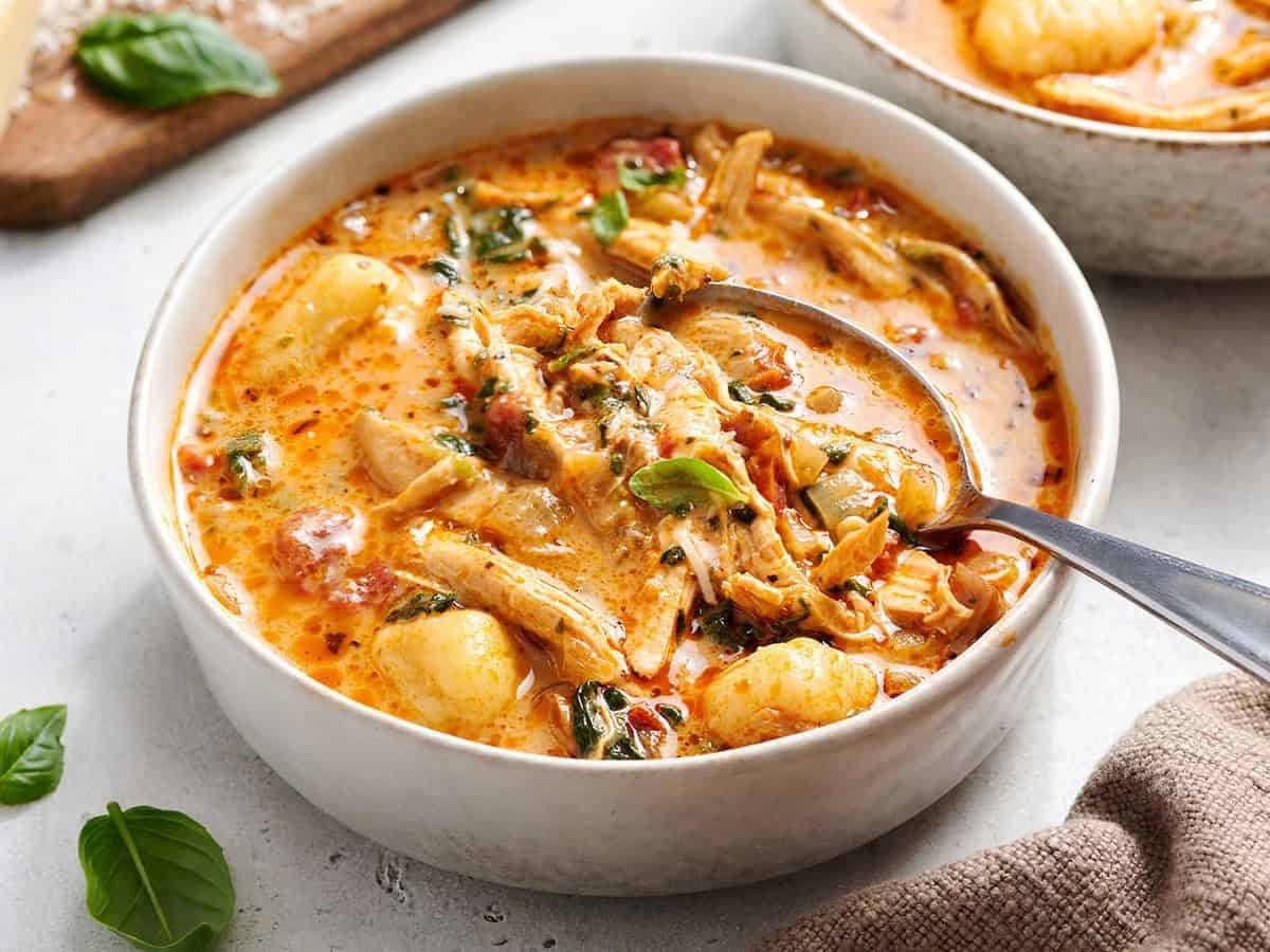 Marry me chicken soup in a white bowl with a spoon, garnished with fresh basil.