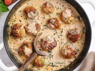 Overhead view of marry meatballs in a skillet with a wooden spoon.