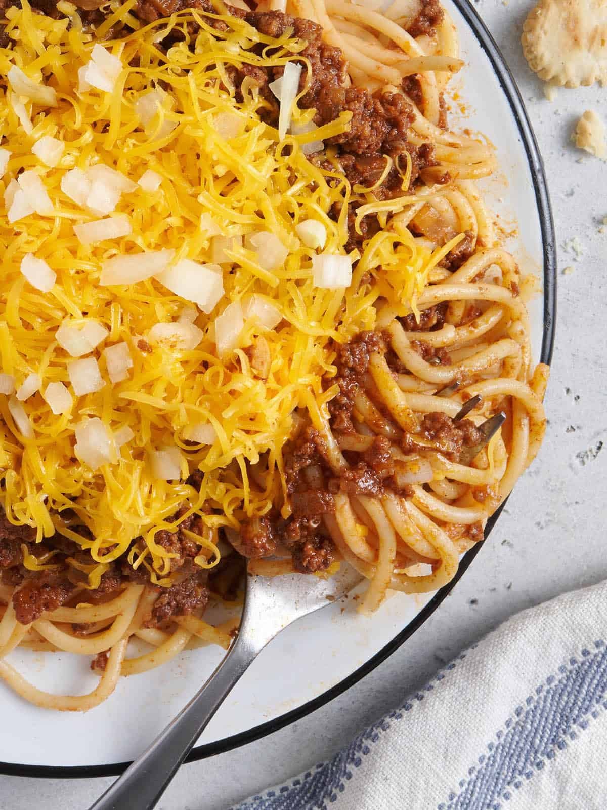 Overhead view of a plate of copycat skyline chili with shredded cheese, diced onions, and a fork.