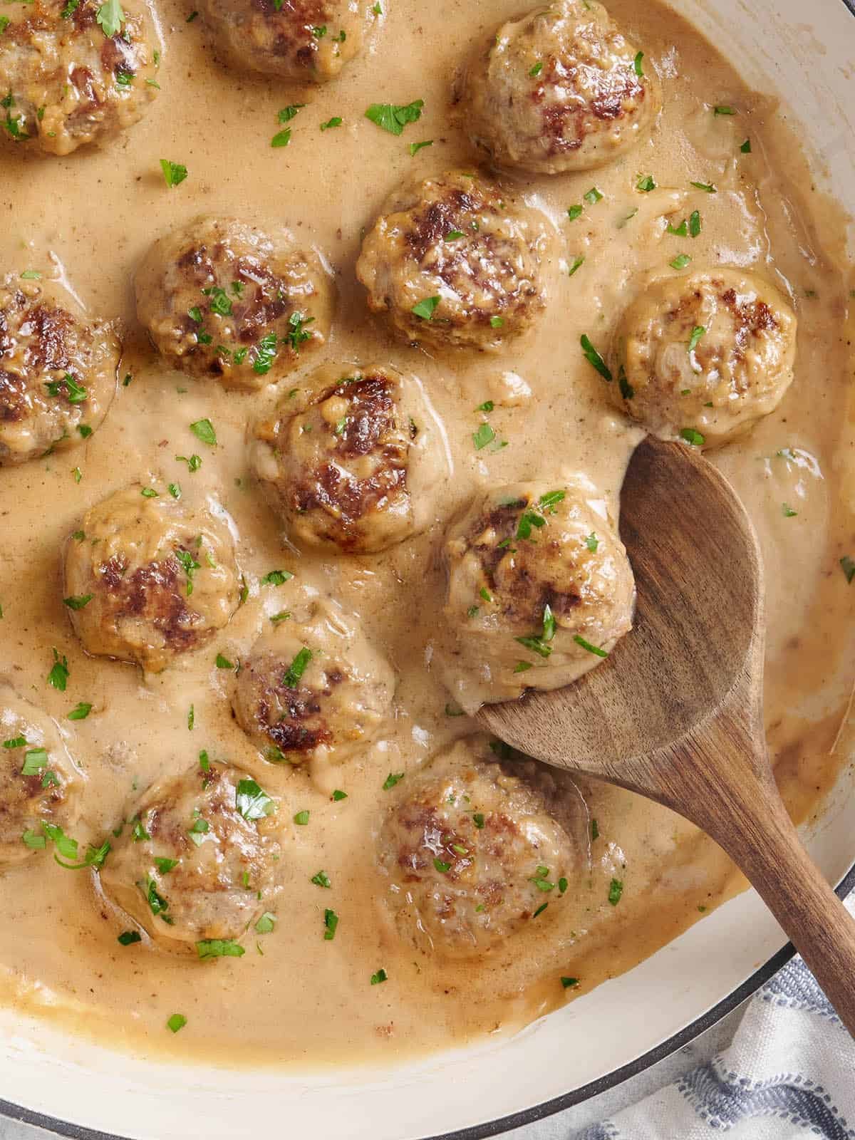 Overhead view of swedish meatballs in a skillet with a wooden spoon.