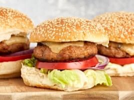 side view of turkey burgers topped with cheese, lettuce, and tomato on buns.