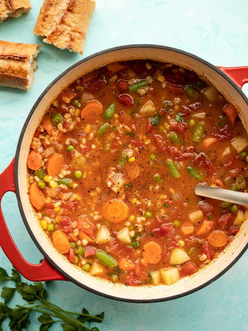 Overhead view of Vegetable Barley Soup in a red pot with bread and parsley on the side