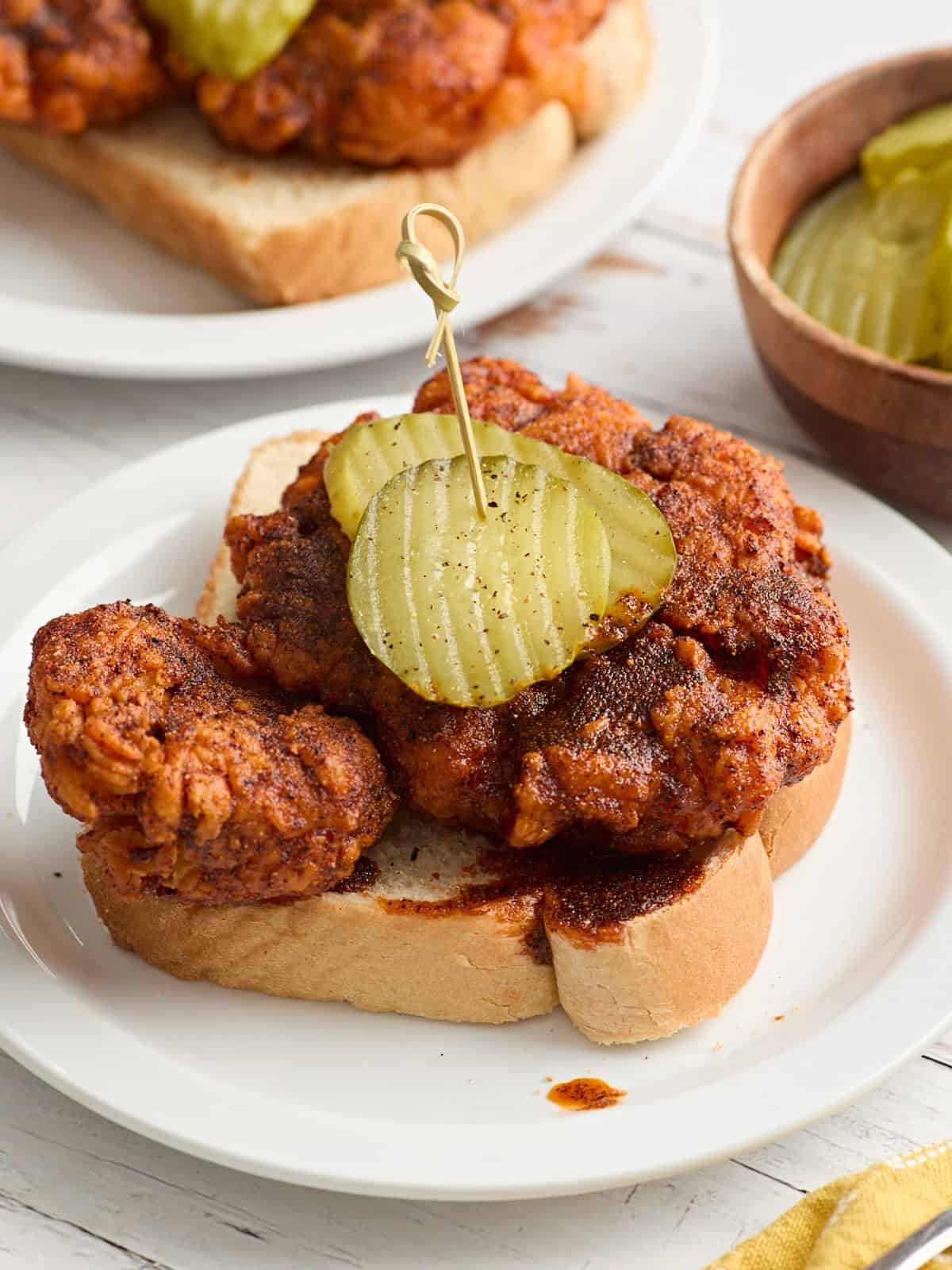 Side view of homemade Nashville hot chicken on a slice of Texas bread on a plate and topped with pickle slices.