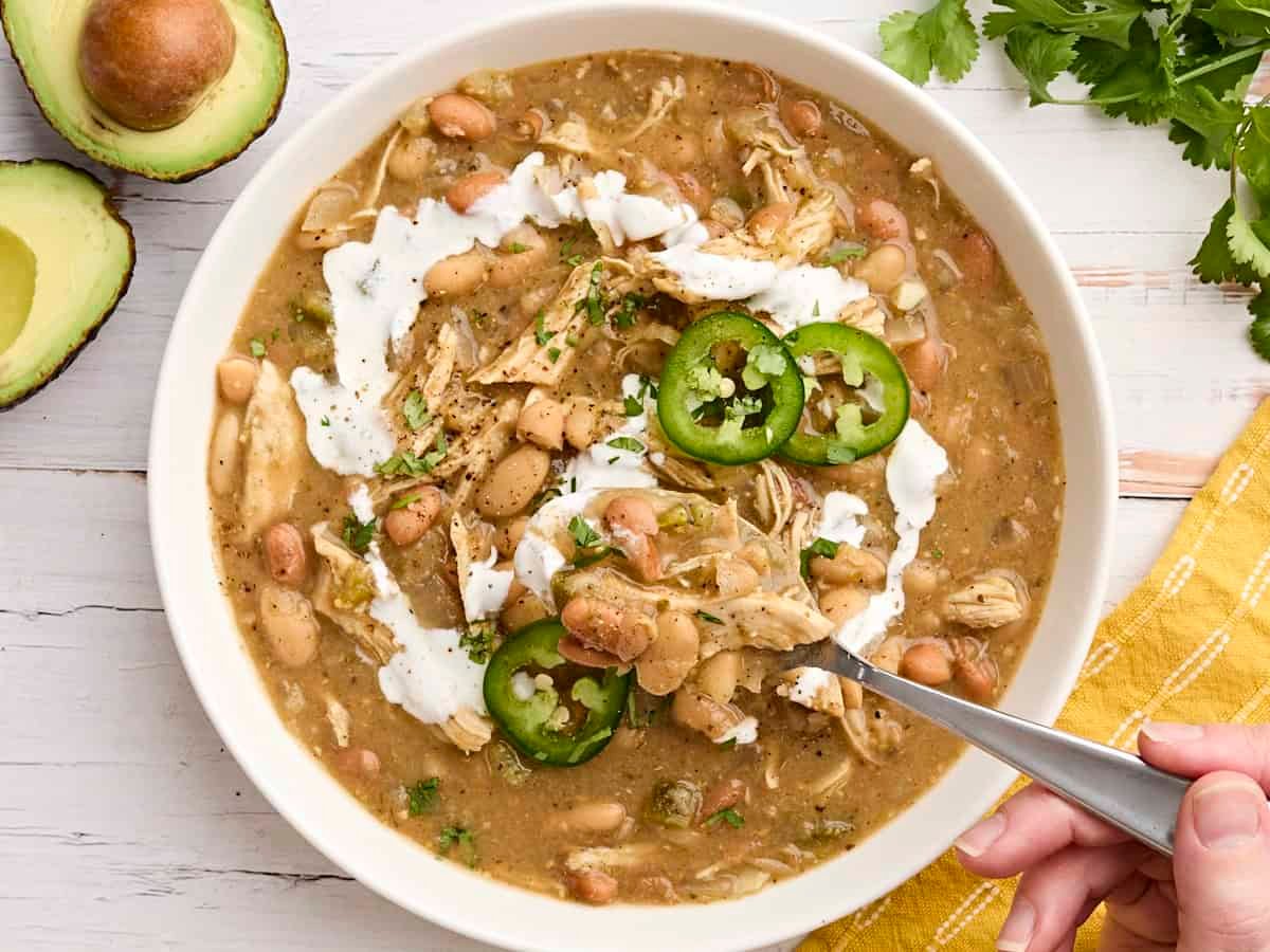 Crockpot white chicken chili in a bowl with a spoon taking some.